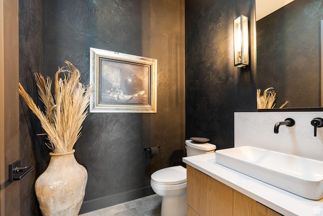 half bathroom with vanity, toilet, and baseboards