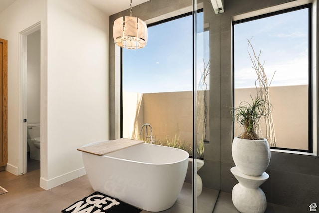 full bathroom with a notable chandelier, a soaking tub, a healthy amount of sunlight, and toilet