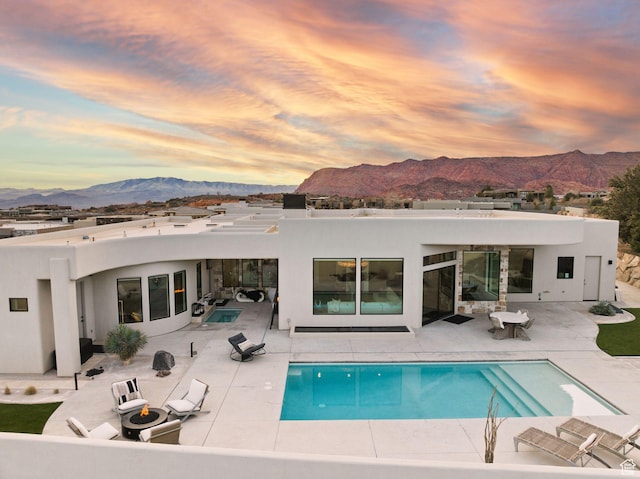 back of property at dusk featuring an outdoor pool, stucco siding, a mountain view, and a patio