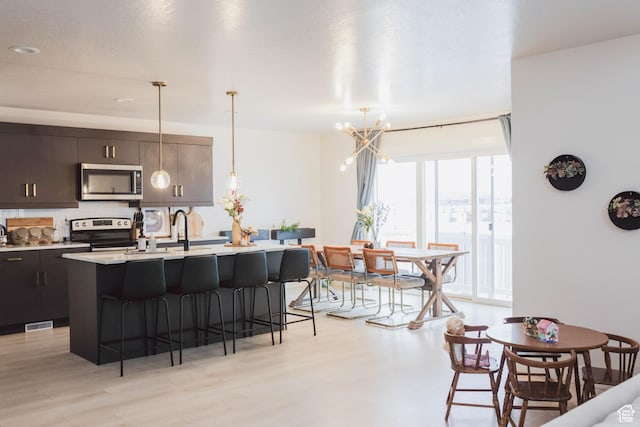 kitchen featuring a kitchen bar, a sink, stainless steel appliances, light countertops, and a chandelier