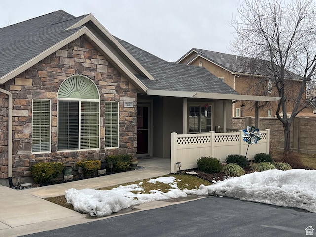 view of front of home featuring stucco siding, stone siding, a shingled roof, and fence