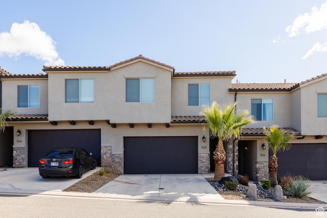 mediterranean / spanish-style home with stucco siding, a tile roof, stone siding, concrete driveway, and an attached garage
