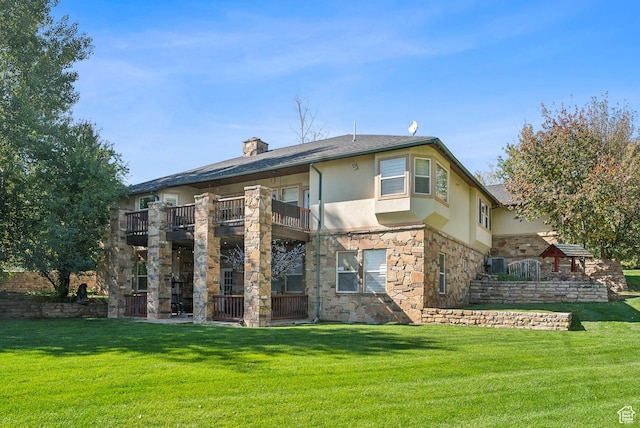 rear view of property with stucco siding, a lawn, a chimney, a balcony, and stone siding