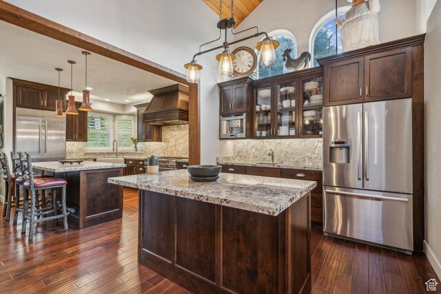 kitchen with dark brown cabinetry, premium appliances, a kitchen island, and premium range hood