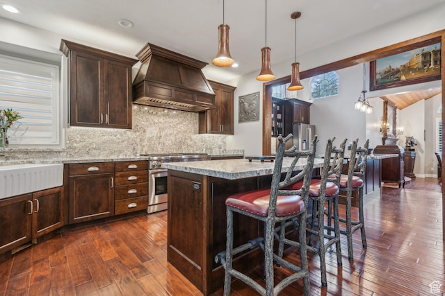 kitchen featuring dark wood-style flooring, decorative backsplash, custom range hood, high end stainless steel range, and a center island