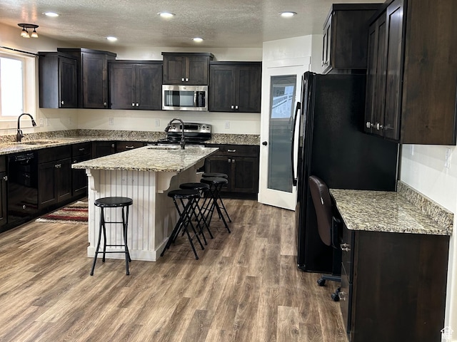 640 S 100 E, Mantua, UT 84324 - kitchen featuring a center island with sink, a kitchen breakfast bar, wood finished floors, black appliances, and a sink