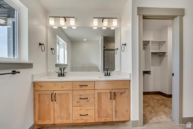 full bath featuring a walk in closet, a shower stall, double vanity, and a sink