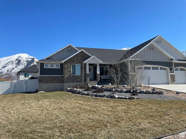craftsman-style home with stone siding, fence, a mountain view, board and batten siding, and a front yard