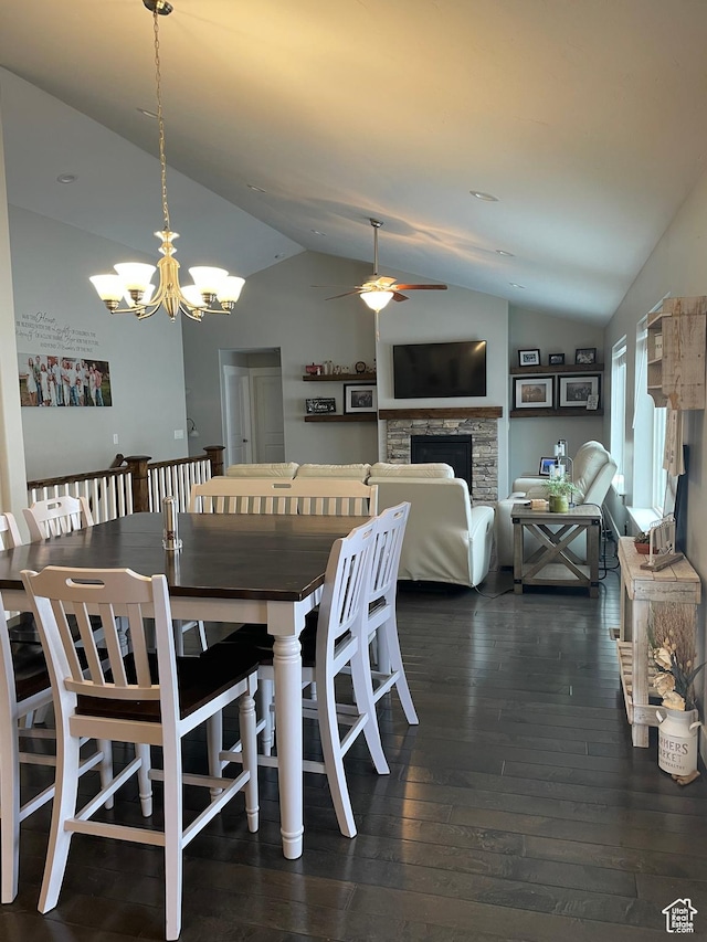 dining room with dark wood-style floors, a stone fireplace, ceiling fan with notable chandelier, and lofted ceiling