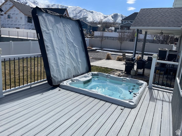 deck with a covered hot tub, a mountain view, and a fenced backyard