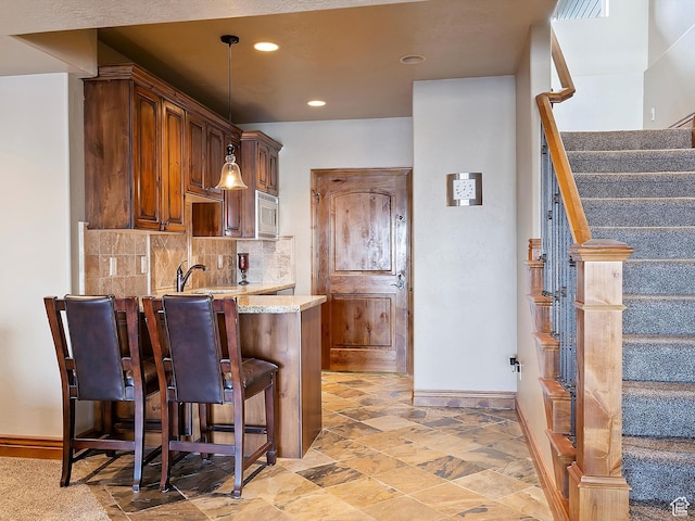 946 S Meadow Lark Ln E, Huntsville, UT 84317 - kitchen featuring light stone counters, a kitchen breakfast bar, a peninsula, stainless steel microwave, and decorative backsplash