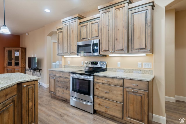 kitchen with arched walkways, appliances with stainless steel finishes, light wood-type flooring, and light stone counters
