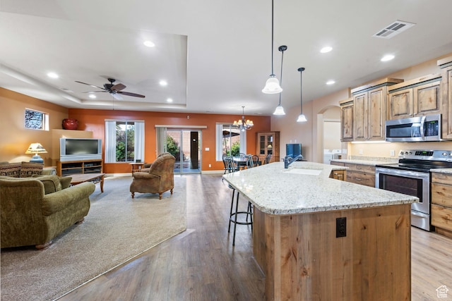 kitchen with arched walkways, a sink, stainless steel appliances, a raised ceiling, and open floor plan
