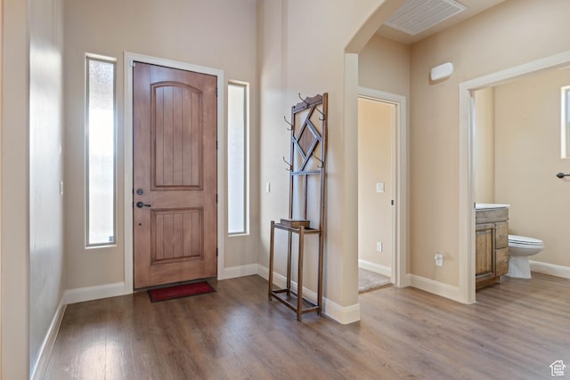 foyer featuring arched walkways, visible vents, baseboards, and wood finished floors
