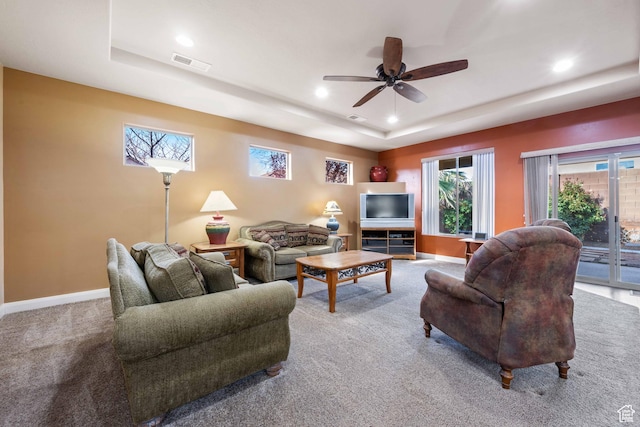 carpeted living area with visible vents, a raised ceiling, baseboards, and a ceiling fan