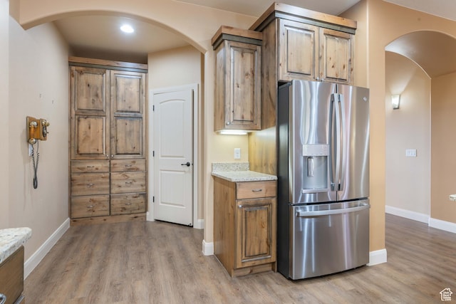 kitchen featuring light stone counters, arched walkways, light wood-style floors, and stainless steel refrigerator with ice dispenser