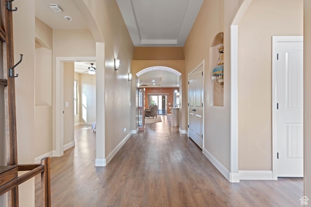 corridor with wood finished floors, arched walkways, and baseboards