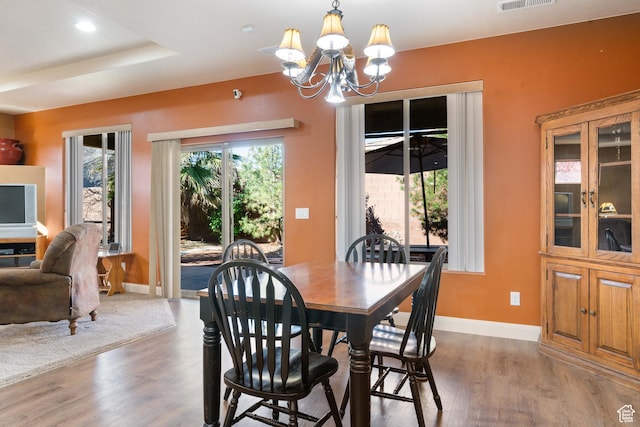 dining area with visible vents, wood finished floors, baseboards, a raised ceiling, and a chandelier