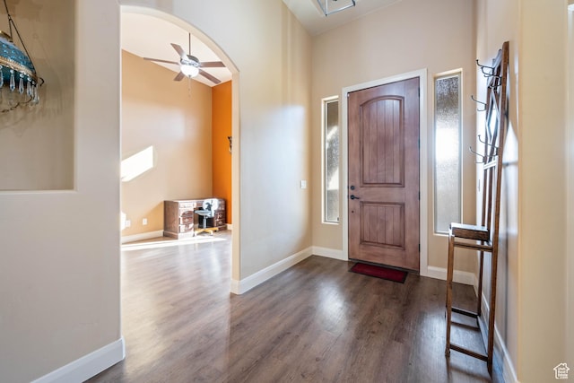 foyer featuring baseboards, arched walkways, and dark wood-type flooring