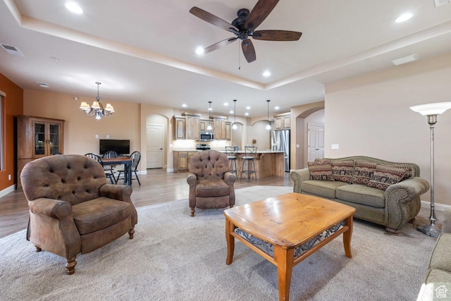 living room featuring visible vents, arched walkways, a raised ceiling, and ceiling fan with notable chandelier