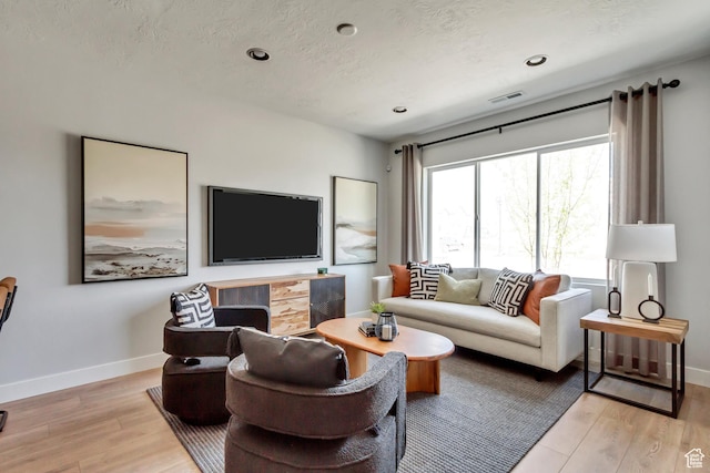 living room featuring baseboards, light wood finished floors, and a textured ceiling