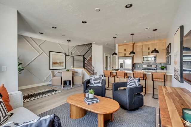 living area featuring a notable chandelier, recessed lighting, light wood-style floors, baseboards, and stairs