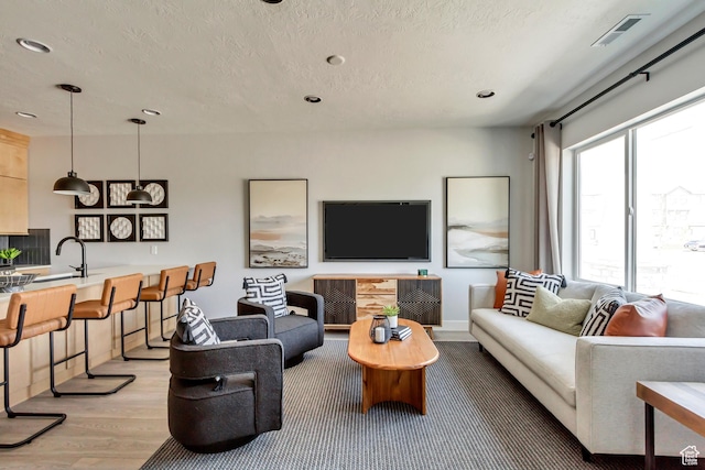 living area with light wood finished floors, visible vents, recessed lighting, and a textured ceiling