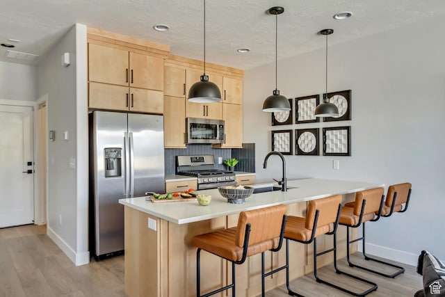 kitchen featuring light brown cabinets, a peninsula, stainless steel appliances, light wood-style floors, and backsplash
