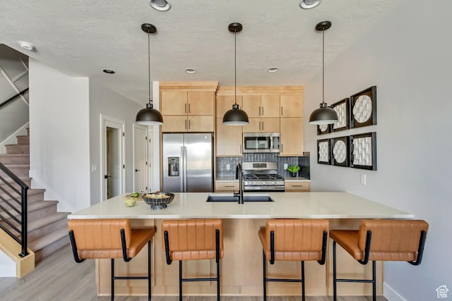 kitchen with a kitchen bar, light brown cabinets, a sink, stainless steel appliances, and decorative backsplash
