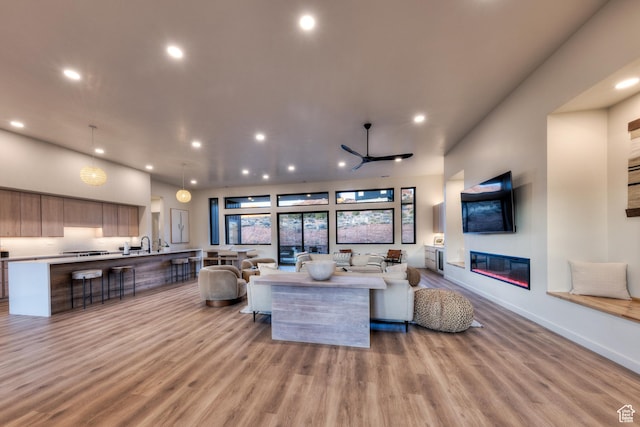 living area featuring recessed lighting, light wood-type flooring, a glass covered fireplace, and a ceiling fan