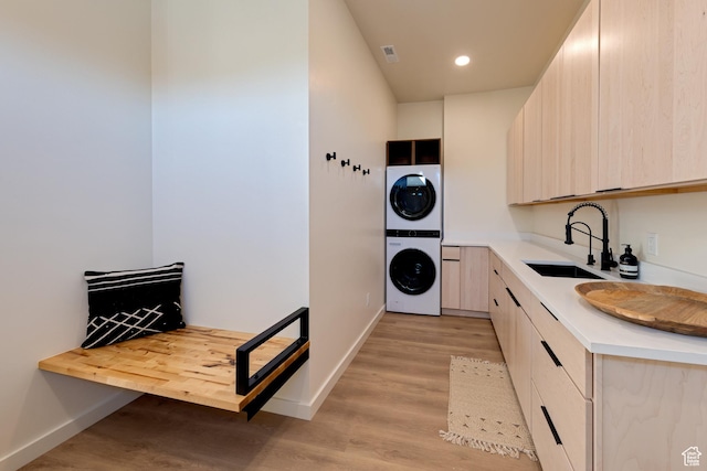 laundry room with light wood-style flooring, a sink, stacked washing maching and dryer, baseboards, and laundry area
