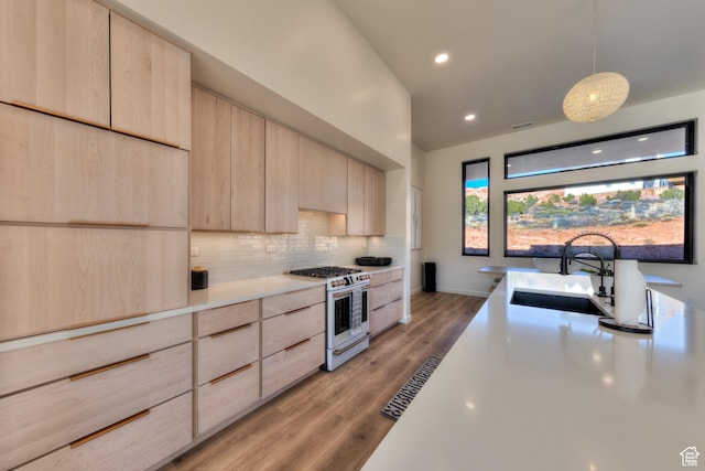 kitchen featuring tasteful backsplash, light brown cabinetry, white range with gas cooktop, modern cabinets, and a sink