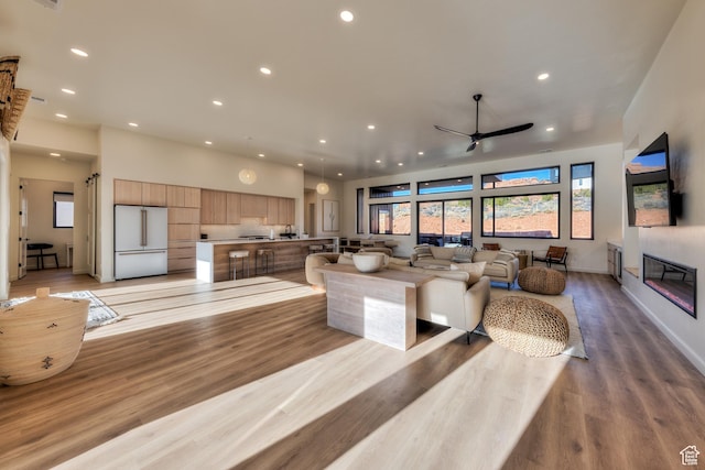 living area with baseboards, light wood-style flooring, recessed lighting, ceiling fan, and a glass covered fireplace