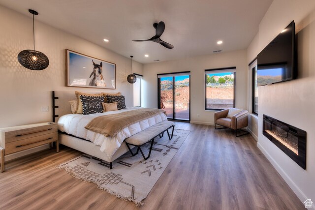 bedroom with wood finished floors, baseboards, recessed lighting, access to exterior, and a glass covered fireplace