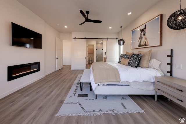 bedroom featuring recessed lighting, baseboards, a barn door, and wood finished floors