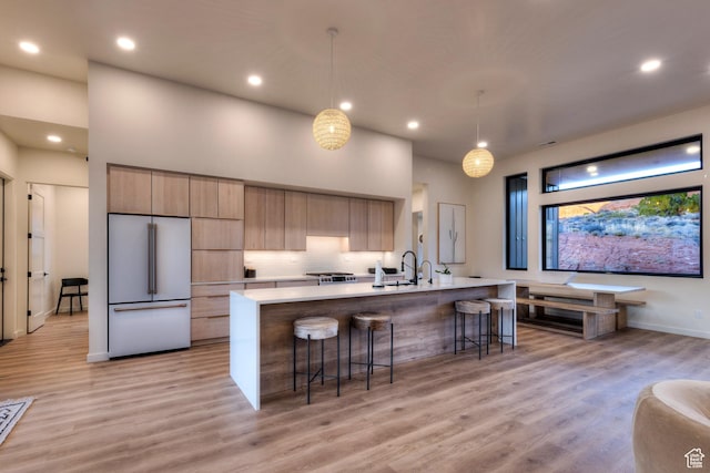 kitchen featuring high end refrigerator, light wood-style flooring, a kitchen breakfast bar, and light countertops