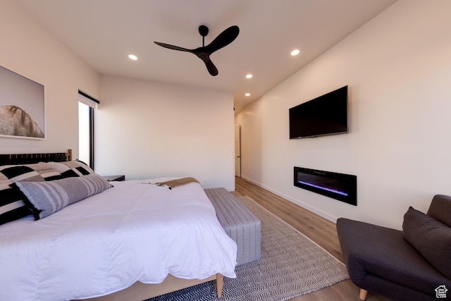 bedroom with a glass covered fireplace, recessed lighting, ceiling fan, and wood finished floors