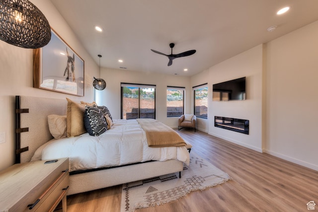 bedroom featuring a glass covered fireplace, recessed lighting, baseboards, and wood finished floors