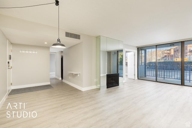 unfurnished living room featuring visible vents, expansive windows, wood finished floors, a fireplace, and baseboards