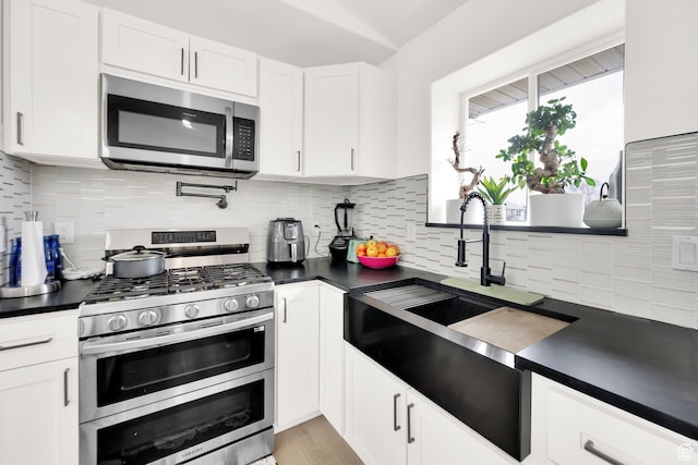 7898 N Tinamous Rd, Eagle Mountain, UT 84005 - kitchen with a sink, dark countertops, white cabinetry, stainless steel appliances, and decorative backsplash
