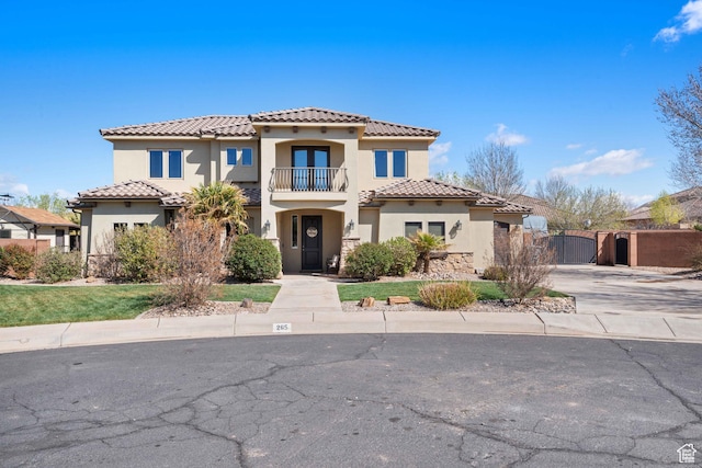 mediterranean / spanish house with a balcony, a gate, stucco siding, concrete driveway, and a tiled roof