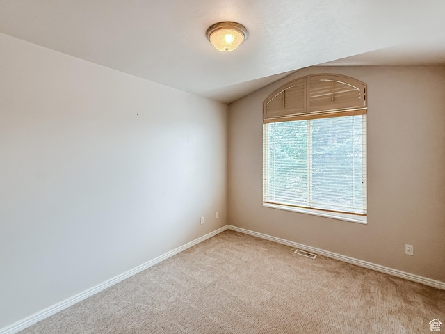 carpeted spare room featuring lofted ceiling, baseboards, and visible vents