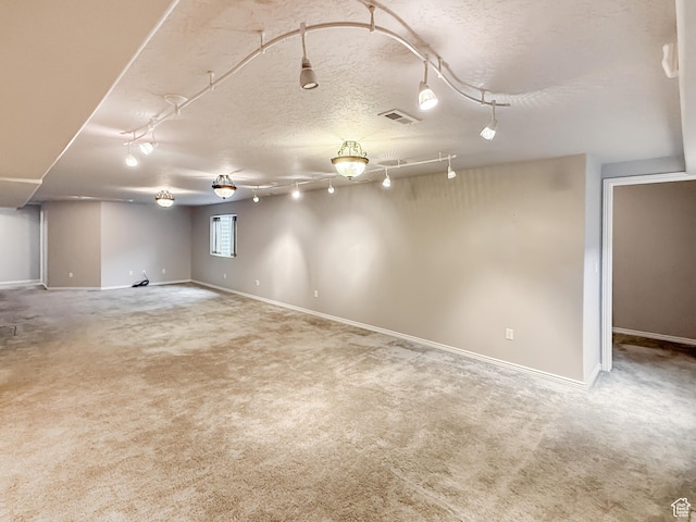 basement featuring baseboards, visible vents, track lighting, a textured ceiling, and carpet flooring