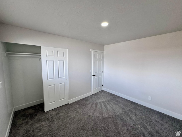 unfurnished bedroom featuring baseboards, a textured ceiling, a closet, and dark colored carpet