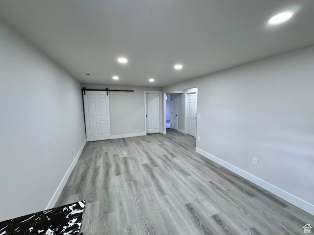 unfurnished bedroom featuring baseboards, a barn door, light wood finished floors, and recessed lighting