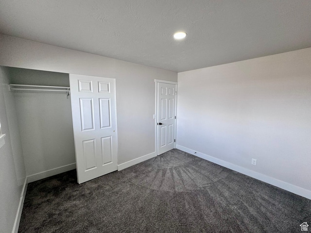 unfurnished bedroom with baseboards, a closet, dark carpet, and a textured ceiling