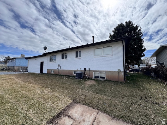 back of house featuring brick siding, central air condition unit, and a yard