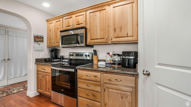kitchen featuring dark stone counters, dark wood-style floors, recessed lighting, arched walkways, and stainless steel appliances