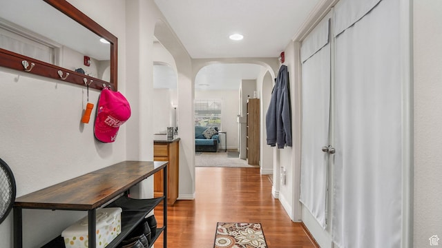 corridor featuring recessed lighting, wood finished floors, arched walkways, and baseboards