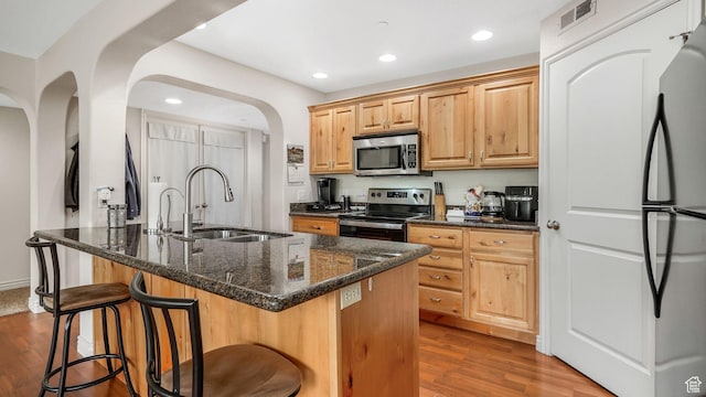 kitchen featuring a breakfast bar area, wood finished floors, arched walkways, stainless steel appliances, and a sink